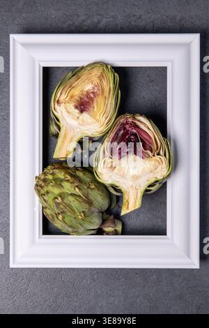 Fresh artichokes displayed in a white frame on dark surface Stock Photo