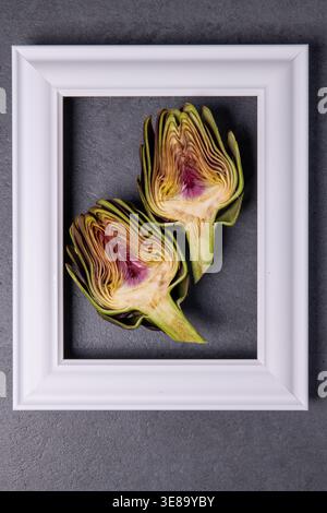 Two artichokes placed in a white frame on gray surface Stock Photo