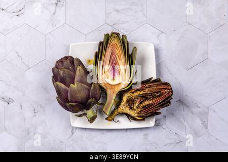 Three artichokes placed on a square plate on marble surface Stock Photo