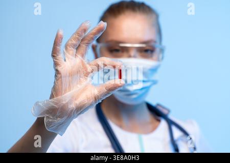 Healthcare professional in mask and gloves holding a red pill, representing medication, treatment, and medical research Stock Photo