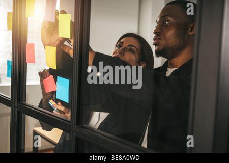 Team members work together on sticky notes in an office setting during afternoon hours to brainstorm ideas and organize tasks Stock Photo