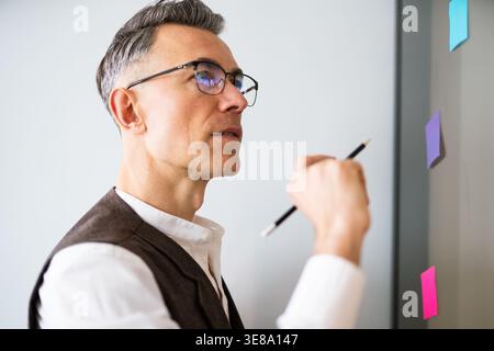 Worker engaged in planning and organizing ideas using colorful sticky notes on a wall during a brainstorming session in an office Stock Photo