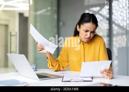 Stressed businesswoman looking at papers with a frustrated expression, managing work and feeling overwhelmed by problems, deadlines, or complex tasks in the modern office Stock Photo