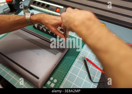 Man repairing laptop computer, using screwdriver to open back panel, focusing on technical maintenance and service at workstation Stock Photo