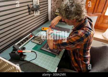 Man actively repairing a laptop computer on a workbench, using a multimeter to diagnose electronic hardware issues and provide tech support Stock Photo