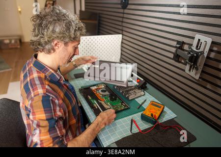 Man carefully disassembling a laptop computer, performing technical maintenance and fixing electronics on a workbench at home Stock Photo