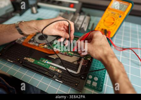 Technician using a multimeter to test circuit board components inside an open laptop, performing electronics repair and maintenance Stock Photo