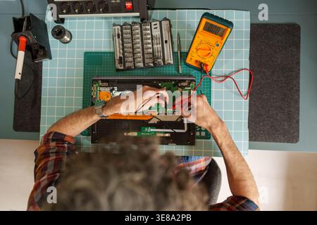 Man troubleshooting an open laptop circuit board, performing electronic repairs and maintenance on a workbench with tools Stock Photo