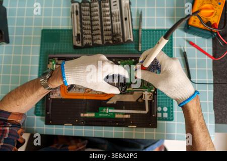Technician hands repairing laptop computer, using a soldering iron and screwdriver to fix electronic components on circuit board Stock Photo