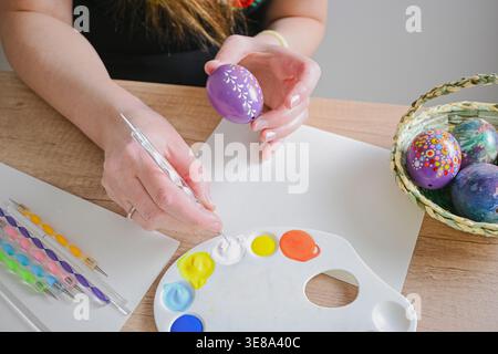 Woman hands painting colorful easter eggs with paint and dotting tools on a wooden table. Stock Photo