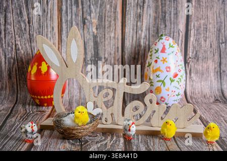 Easter decorations featuring a wooden sign with bunny ears, chicks, and colorful eggs on wood background. Stock Photo