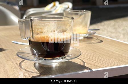 Close up view of two glass espresso coffee cups on a wooden table at an outdoor cafe in the sun algarve portugal Stock Photo