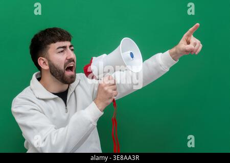 Man actively yelling and speaking through a megaphone while pointing, standing in front of a chroma key green background Stock Photo