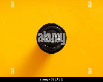 Black plastic coffee cup lid with pollution message on yellow background, raising eco awareness Stock Photo