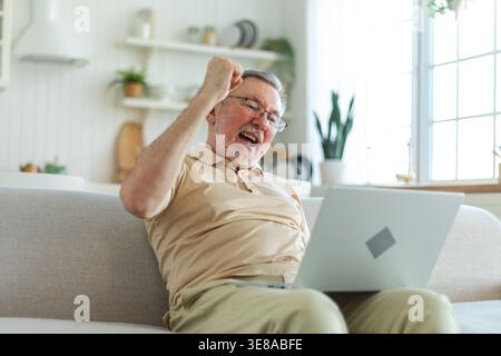 Excited middle aged senior man euphoric winner. Older mature grandfather looking at laptop reading great news getting good result winning online bid feeling amazed. Winning gesture Stock Photo