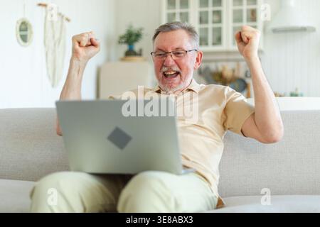Excited middle aged senior man euphoric winner. Older mature grandfather looking at laptop reading great news getting good result winning online bid feeling amazed. Winning gesture Stock Photo