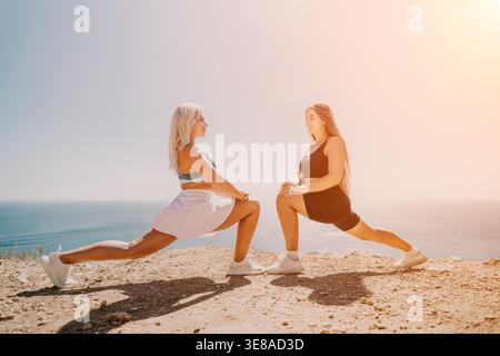 Women stretching cliff exercise where two young athletes perform lunges by the sea on a sunny summer day Stock Photo