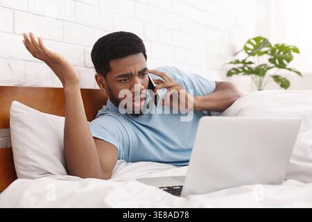 Angry man having problems with laptop talking on mobile phone Stock Photo