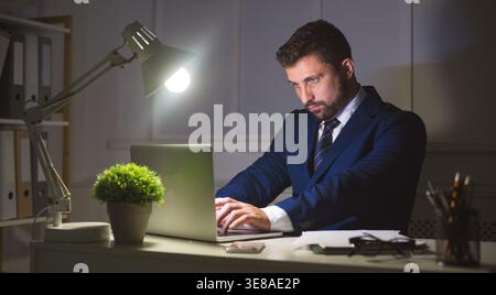Businessman working on laptop in dark office Stock Photo
