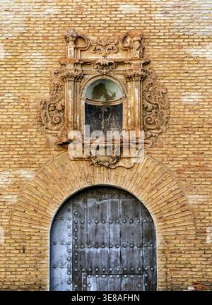 Ornate baroque stone window niche above arched wooden door on aged brick wall, historic architecture facade detail, weathered textures. Stock Photo