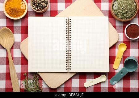 Recipe book and different spices on checkered tablecloth, flat lay Stock Photo