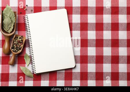 Recipe book and different spices on checkered tablecloth, flat lay. Space for text Stock Photo