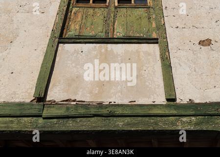 Close-up of a dilapidated facade showing cracked plaster and decaying green painted wooden window elements Stock Photo