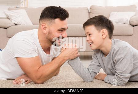 Father and Son Compete in Arm Wrestling While Playing on the Living Room Floor Stock Photo