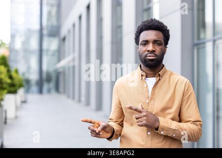 Young man standing outdoors in an urban environment, looking directly forward while confidently gesturing with both hands, indicating a choice or showing a path Stock Photo