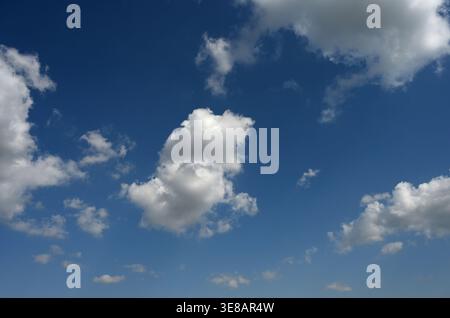 Partly cloudy blue sky with scattered white clouds and a smooth gradient from light blue at the bottom to dark blue at the top in natural lighting Stock Photo