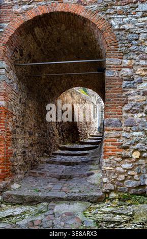 Stone staircase leading through an arched passageway in an ancient stone wall, with weathered bricks and uneven steps visible in a historic setting in Stock Photo