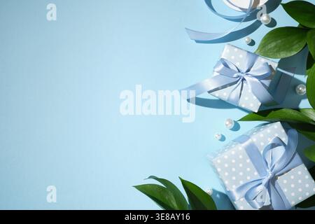 Blue gift boxes with ribbon bows, pearls and green leaves on pastel blue background Stock Photo