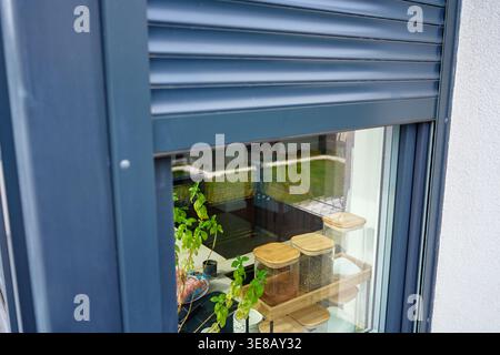 Close up of residential window with partially closed roller shutter on house facade. Exterior detail of modern home. Privacy, security and contemporary architecture concept Stock Photo