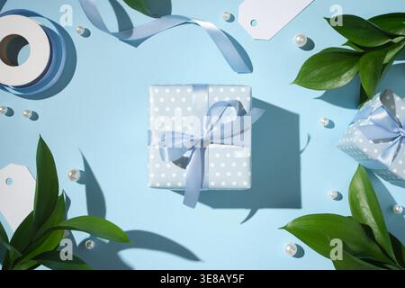 Elegant blue gift box with ribbon bow, pearls and green leaves on pastel background. Stock Photo