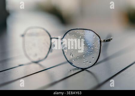 Eyeglasses raindrops table pair of round glasses with water droplets on lenses resting on a wooden surface after rain Stock Photo