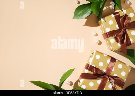 Gift boxes with polka dots, brown ribbons, green leaves, and pearls on a beige background. Copyspace Stock Photo