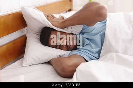 Young man in bed hiding under pillow Stock Photo