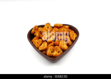 Crispy, flavorful triangular chips in a heart-shaped bowl against a wooden background, a delicious and appetizing food snack. Stock Photo
