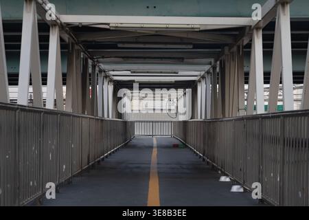 Bangkok, thailand - Apr 5, 2022 - Framed by a symmetrical array of weathered white trusses, this industrial pedestrian overpass stretches forward in a Stock Photo