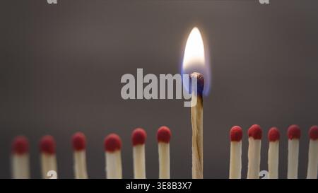Matchsticks Arranged in a Line With One Matchstick Burning Brightly in the Center Stock Photo