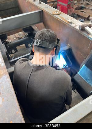 Back view of a professional welder working on a large steel structure in a workshop. Stock Photo