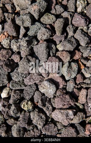 Top-down vertical view of dark porous lava rock gravel. Detailed volcanic stone texture with rough, weathered surfaces for landscaping backgrounds. Stock Photo
