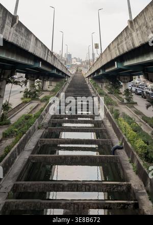 Bangkok, Thailand - Apr 5,  2022 - Framed by twin concrete overpasses, a weathered utility span recedes in sharp perspective toward a distant city sky Stock Photo