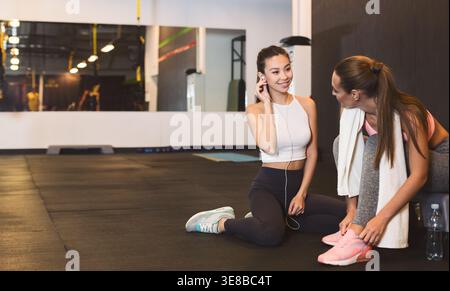 Women Engage in Conversation While Exercising in a Gym Setting During the Day Stock Photo