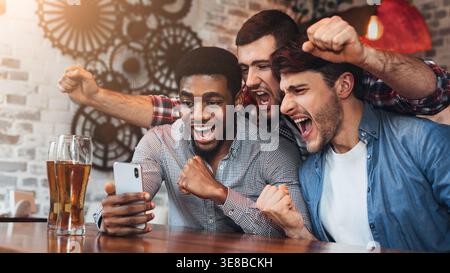 Diverse football fans watching football on smartphoner in pub Stock Photo