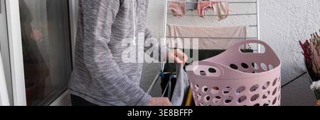 A 50-year-old man is hanging washed clothes on his balcony. He carefully places each item on the drying rack. The laundry has bright colors and fresh Stock Photo