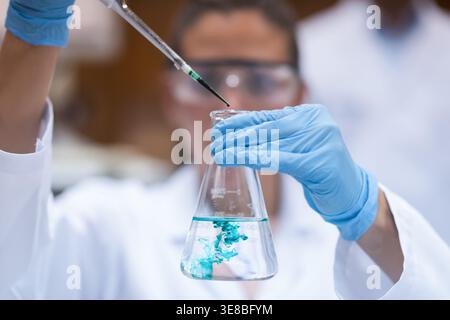 Young doctor in lab adding reagent to flask with pipette during medical testing procedure Stock Photo
