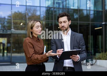 Two business colleagues working together, analyzing important contract documentation and collaborating on a new corporate project outside a modern office building Stock Photo
