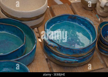 Close up of handmade ceramic bowls with blue glaze stacked on wooden surface, showing artisan craftsmanship and organic shapes suitable for kitchenwar Stock Photo