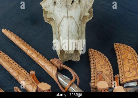 Close up of animal skull with handmade leather knife sheaths featuring carved patterns, arranged in a rustic composition highlighting traditional craf Stock Photo